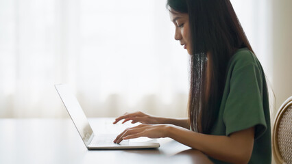 Wall Mural - Young asian woman working at home. Female using computer laptop on desk at house