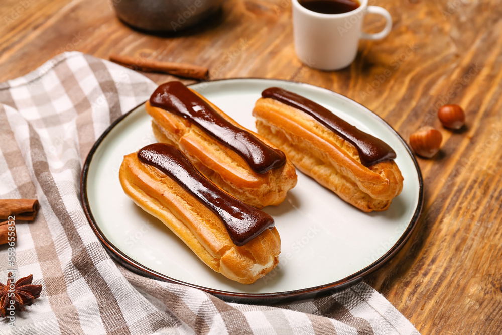 Plate with tasty chocolate eclairs on wooden table