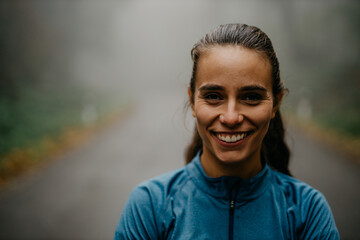 Wall Mural - Portrait of a smiling confident female personal trainer who is standing with arms crossed in a sports outfit during the morning jogging in the forest.