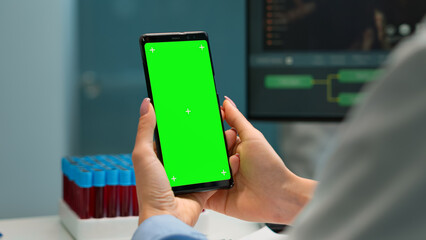 Wall Mural - close up of doctor's hand holding phone with green screen sitting at desk in biological laboratory w