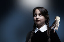 Portrait Of Little Girl With Wednesday Costume During Halloween. Serious Expression And Dark Atmosphere With Dark Background.
