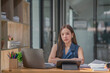 © Songsak C - Asian businesswoman looking at the camera, an attractive businesswoman working on a laptop in her workstation office.