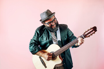 Happy bearded man playing acoustic guitar on pink background.