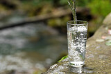 Fototapeta Łazienka - Fresh water pouring into glass on stone near river. Space for text