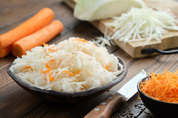 Bowl of sour cabbage, pickled sauerkraut. Fermented cabbage, coleslaw salad. Chopped cabbage on a cutting board and carrots for making sauerkraut on background. Healthy food, diet food.