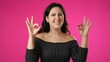 © Robert Peak - Portrait of pretty young hipster woman 20s giving okay gesture smiling happy isolated on pink background studio portrait with copy space