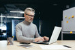 © Liubomir - Portrait of a senior gray-haired man, financial analyst, freelancer, banker is working in the office at a table with a laptop.