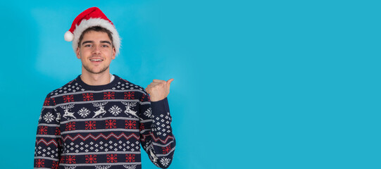 Wall Mural - isolated young man in christmas clothes and santa claus hat on blue background