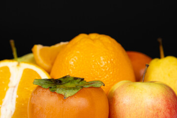 Fruits of orange and yellow colors - apples, persimmons and oranges on a black background