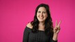 © Robert Peak - Portrait of attractive happy young woman 20s smiling and giving peace or victory sign gesture with hands isolated on pink background.