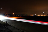 Fototapeta Las - Long exposure of cars passing on road next to airport at night.