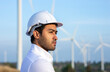 © Pituk - Portrait of young engineering man wearing white safety helmet standing on wind turbine field background.
