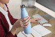 © New Africa - Woman holding thermos bottle at workplace, closeup.