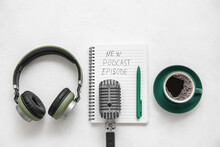 Notebook with text NEW PODCAST EPISODE, microphone, coffee cup and headphones on white background