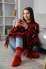 Sticker - Young woman in warm plaid with glass cup of tea at home