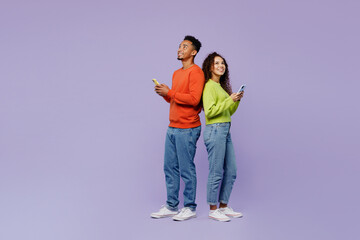 Wall Mural - Full body side view young couple two friends family man woman of African American ethnicity wear casual clothes together hold use mobile cell phone look overhead isolated on plain purple background.