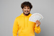 © ViDi Studio - Young rich wealthy smiling Indian man 20s he wear casual yellow hoody hold in hand fan of cash money in dollar banknotes isolated on plain grey background studio portrait. People lifestyle portrait.