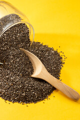 Wall Mural - Healthy breakfast, Chia seeds are pouring out from glass jar with wood spoon over yellow background