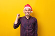 © Sewupari Studio - Excited young Asian man in Santa hat raising hands up, celebrating success on yellow studio background. Happy New Year 2023 celebration merry holiday concept