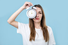 Sleepy Young Woman Covering Her Eye With Alarm Clock On Blue Background