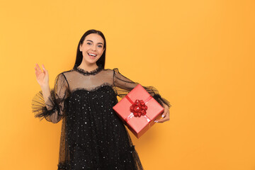 Canvas Print - Happy young woman in festive dress with gift box on orange background, space for text