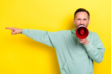 Poster - Photo of grey hair angry man businessman wear khaki sweatshirt hold loud speak finger point empty space isolated on yellow color background