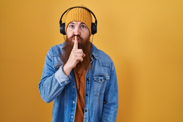 Wall Mural - Caucasian man with long beard listening to music using headphones asking to be quiet with finger on lips. silence and secret concept.