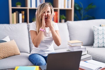 Canvas Print - Young blonde woman studying using computer laptop at home shouting angry out loud with hands over mouth