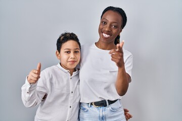 Young mother and son standing together over white background pointing fingers to camera with happy and funny face. good energy and vibes.