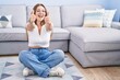 © Krakenimages.com - Young caucasian woman sitting on the floor at the living room approving doing positive gesture with hand, thumbs up smiling and happy for success. winner gesture.