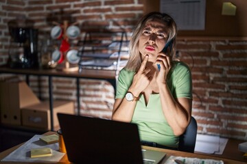 Poster - Young beautiful woman working at the office at night speaking on the phone thinking concentrated about doubt with finger on chin and looking up wondering