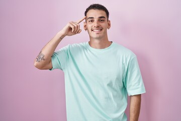 Wall Mural - Handsome hispanic man standing over pink background smiling pointing to head with one finger, great idea or thought, good memory