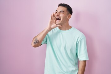 Wall Mural - Handsome hispanic man standing over pink background shouting and screaming loud to side with hand on mouth. communication concept.