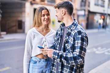 Wall Mural - Young man and woman couple smiling confident using smartphone at street