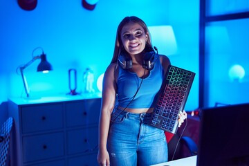 Canvas Print - Young blonde woman playing video games with smartphone holding keyboard looking positive and happy standing and smiling with a confident smile showing teeth