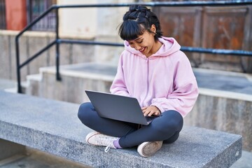 Wall Mural - Young woman using laptop sitting on bench at street