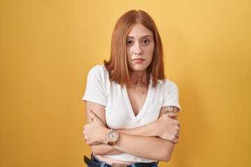 Poster - Young redhead woman standing over yellow background shaking and freezing for winter cold with sad and shock expression on face