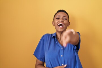 Sticker - African american woman standing over yellow background laughing at you, pointing finger to the camera with hand over body, shame expression