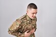 © Krakenimages.com - Young man wearing camouflage army uniform with hand on stomach because indigestion, painful illness feeling unwell. ache concept.