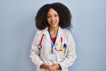 Wall Mural - Young african american woman wearing doctor uniform and stethoscope with hands together and crossed fingers smiling relaxed and cheerful. success and optimistic
