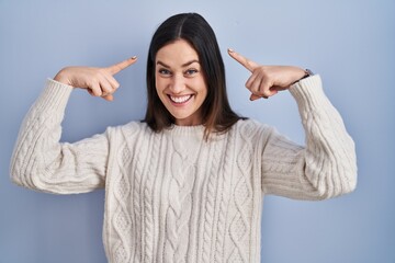 Sticker - Young brunette woman standing over blue background smiling pointing to head with both hands finger, great idea or thought, good memory