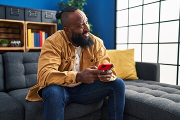 Poster - Young african american man using smartphone sitting on sofa at home