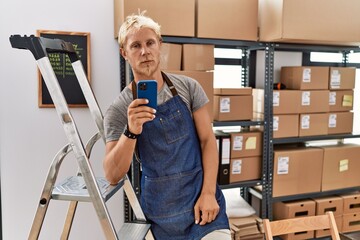 Wall Mural - Young blond man using smartphone working at storehouse looking sleepy and tired, exhausted for fatigue and hangover, lazy eyes in the morning.