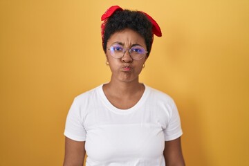 Poster - Young african american woman standing over yellow background puffing cheeks with funny face. mouth inflated with air, crazy expression.