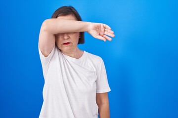 Canvas Print - Middle age hispanic woman standing over blue background covering eyes with arm, looking serious and sad. sightless, hiding and rejection concept