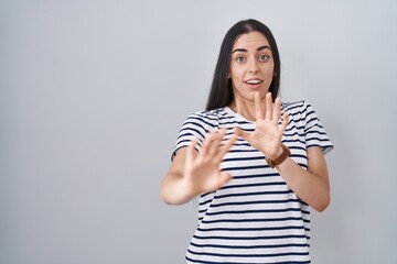 Sticker - Young brunette woman wearing striped t shirt afraid and terrified with fear expression stop gesture with hands, shouting in shock. panic concept.