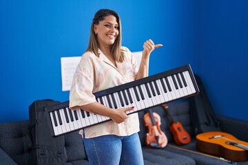 Sticker - Blonde woman holding piano keyboard pointing thumb up to the side smiling happy with open mouth