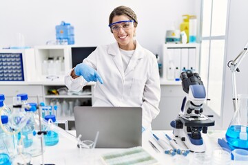 Poster - Young hispanic woman wearing scientist uniform working at laboratory smiling happy pointing with hand and finger