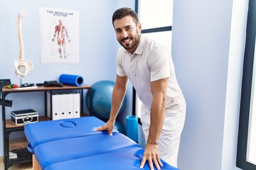 Poster - Young hispanic man wearing physiotherapist uniform standing at clinic