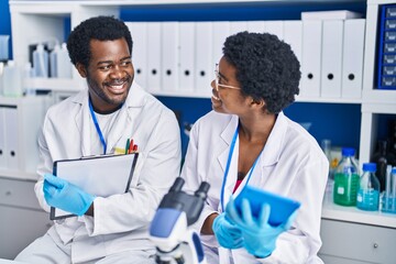 Canvas Print - African american man and woman scientists using touchpad write on document at laboratory